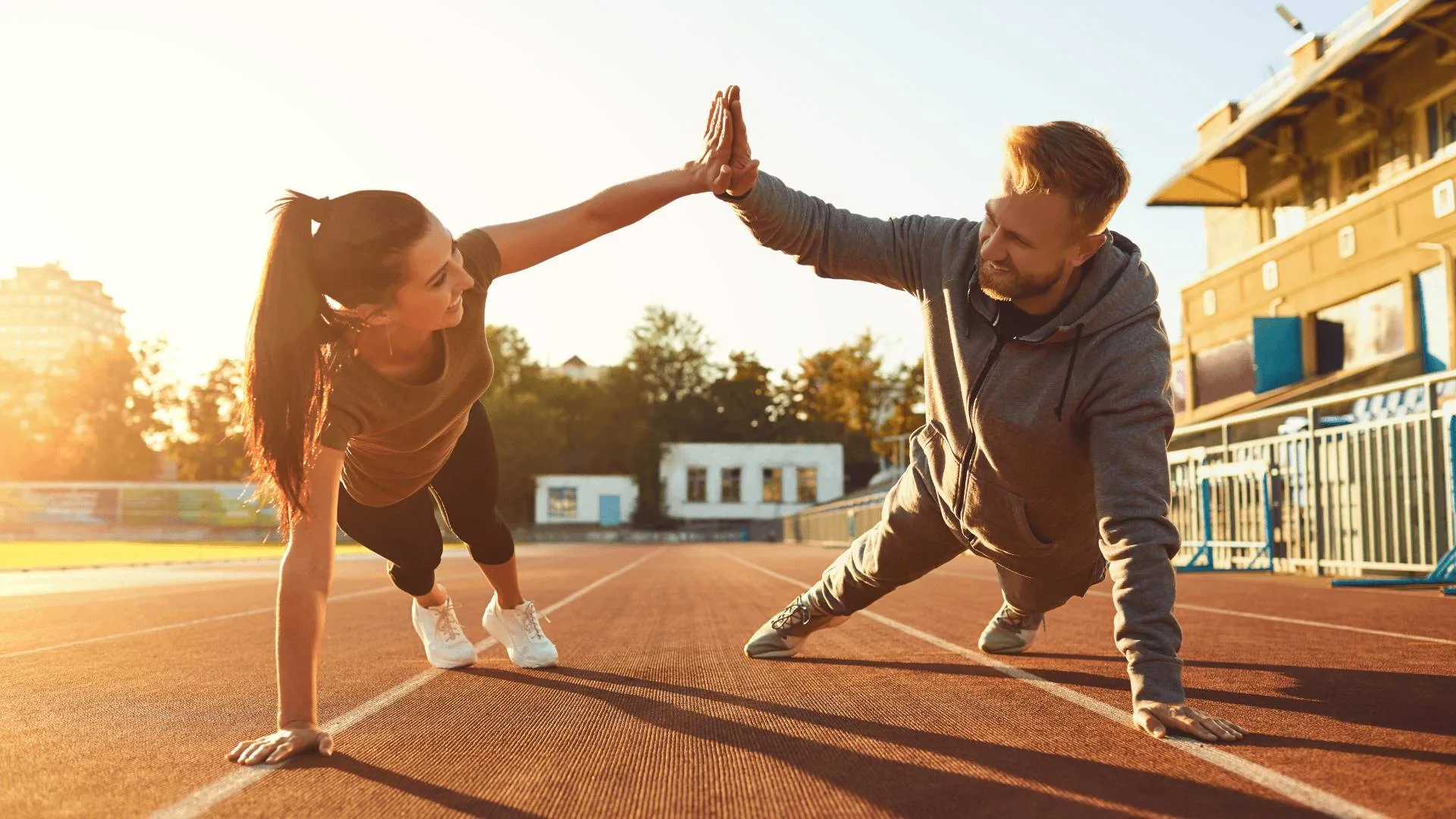 Fit couple doing plank high-five on running track during workout, symbolising strength and fitness from Emsculpt body contouring